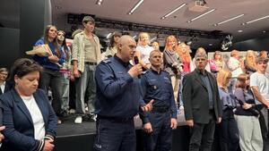 Uczestnicy wydarzenia stojący na stenie, przed scena zaproszeni goście przemawiają.