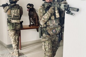 Umundurowani policjanci z bronią w ręku i pies policyjny w budynku podczas ćwiczeń.