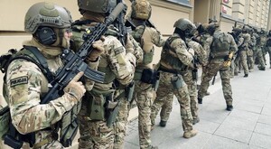 Umundurowani policjanci z bronią w ręku przed budynkiem Uniwersytetu łódzkiego podczas ćwiczeń.