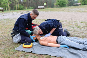 Umundurowani policjanci biorący udział w pozorowanej sytuacji kwalifikowanej pierwszej pomocy osobie wyciągniętej z wody po podtopieniu.