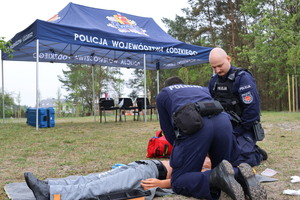 Umundurowani policjanci biorący udział w pozorowanej sytuacji kwalifikowanej pierwszej pomocy osobie wyciągniętej z wody po podtopieniu.