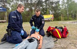Umundurowani policjanci biorący udział w pozorowanej sytuacji kwalifikowanej pierwszej pomocy osobie wyciągniętej z wody po podtopieniu.