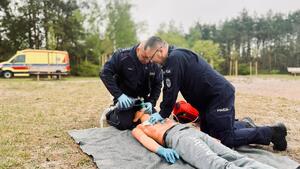 Umundurowani policjanci biorący udział w pozorowanej sytuacji kwalifikowanej pierwszej pomocy osobie wyciągniętej z wody po podtopieniu.