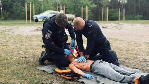 Umundurowani policjanci biorący udział w pozorowanej sytuacji kwalifikowanej pierwszej pomocy osobie wyciągniętej z wody po podtopieniu.