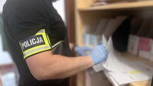 Nieumundurowany policjant z opaską z napisem Policja przegląda dokumentacje.