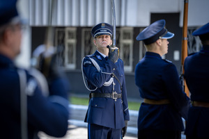 Policjant umundurowany podczas uroczystości z szablą w dłoni.