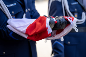 Funkcjonariusz Policji trzymający w reku złożoną flagę.