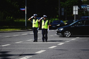 Policjanci umundurowani kierujący przekazujący sobie wartę kierowania ruchem na skrzyżowaniu.