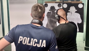 Policjant z funkcjonariuszem prowadzącym strzelanie przy tarczy strzeleckiej liczący punkty.