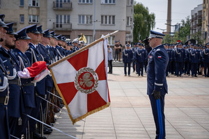 Umundurowany funkcjonariusz oddający honor przed pocztem sztandarowym.