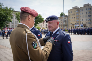 Umundurowany funkcjonariusz wojska wręczający medal funkcjonariuszowi policji.
