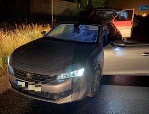 Grafitowy samochód osobowy z otwartymi drzwiami, za nim znajduje się inne auto.