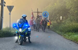 Policjant na motocyklu, za nim idąca kolumna pielgrzymów.
