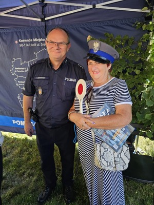 Policjant wraz z kobietą, która ma założoną czapkę policyjną.