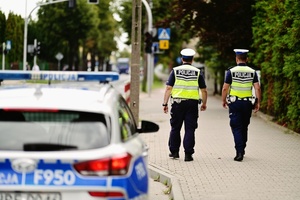 Radiowóz obok policjanci, którzy dokonują lustracji oznakowań.