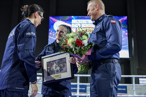 Dwie policjantki, jedna ze zdjęciem oraz Komendant Wojewódzki Policji w Łodzi z kwiatami.