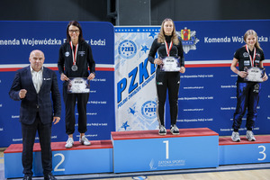 Trzy zawodniczki na podium z medalami i dyplomami i wręczający medale.