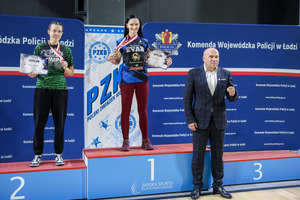 Dwie zawodniczki z medalami i dyplomami na podium pierwszego i drugiego miejsca z wręczającym medale.