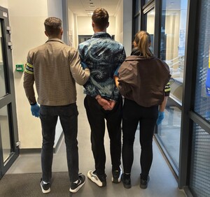 Nieumundurowani policjanci stoją z zatrzymanym mężczyzną.