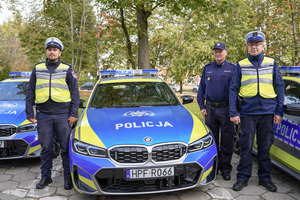 Umundurowani policjanci stoją przy oznakowanym radiowozie.
