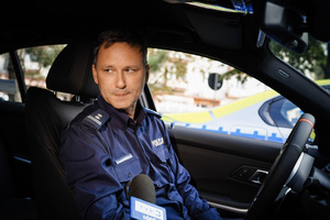 Umundurowany policjant siedzący wewnątrz radiowozu.