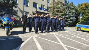 Policjanci oddają hołd zmarłemu Koledze. Umundurowani funkcjonariusze stoją przy radiowozach.