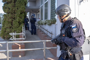 Umundurowani policjanci w hełmach stoją przy wejściu do budynku.