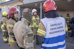 Policjant Samodzielnego Pododdziału Kontrterrorystycznego Policji stoi obok strażaków.