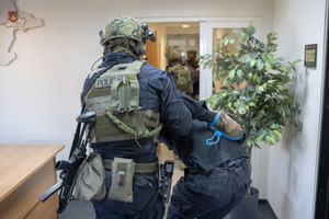 Policjant z Samodzielnego Pododdziału Kontrterrorystycznego Policji wyprowadza zamaskowanego napastnika.