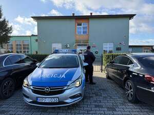 Policjant na tle oznakowanego radiowozu patrolujący teren wokół szkoły.