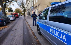 Policjanci na tle oznakowanego radiowozu patrolują tereny wokół szkół.