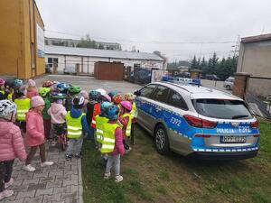 Dzieci w kamizelkach odblaskowych przy radiowozie.