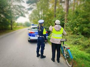 Seniorka w kamizelce odblaskowej przy rowerze, policjantka ruchu drogowego z nią rozmawia.