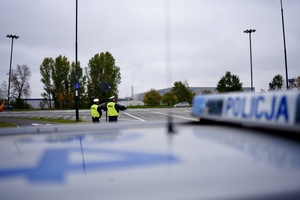 Umundurowani funkcjonariusze Policji stojący przy radiowozie.