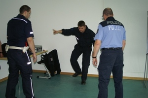 Zdjęcie trzech uczestników zajęć w trakcie ćwiczeń - dwóch stoi tyłem i jeden przodem