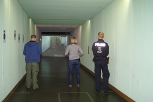Zdjęcie trojga uczestników zajęć w sali ćwiczebnej w formie korytarza z wyświetlonym na jego końcu na ekranie obrazem obiektu