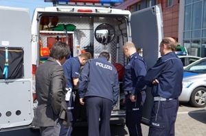 Zdjęcie pięciu uczestników imprezy przez otwartym tyłem policyjnego samochodu typu van (widać wyposażenie)