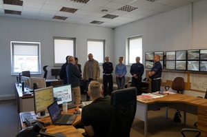 Zdjęcie grupy uczestników stojących w pomieszczeniu stanowiska kierowania - widać ścianę z monitorami i dyżurnego przy stanowisku