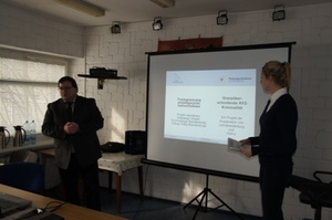 Zdjęcie dwojga prelegentów w sali wykładowej po bokach ekranu z wyświetloną prezentacją