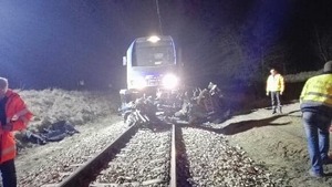 Tory kolejowe, pociąg, z przodu zgnieciony samochód, obok policjanci.