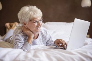 seniorka leży na łóżku i przegląda Internet