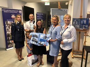 pamiątkowe zdjęcie małżeństwa z dzieckiem i ich praca - książeczką  interaktywna,obok policjantka w mundurze.