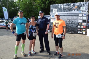 3 biegaczy w strojach sportowych i umundurowany policjant pozują do zdjęcia.