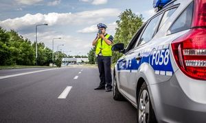umundurowany policjant w kamizelce odblaskowej stoi przy radiowozie przy drodze