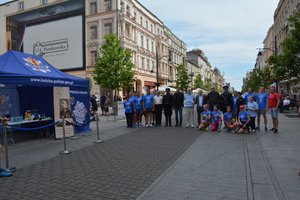 pamiątkowe zdjęcie na środku ulicy Piotrkowskiej , przy starcie stoi cześć uczestników biegu oraz organizatorzy i sponsor