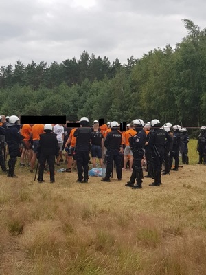 widać policjantóiw z OPP w Łodzi, którzy otoczyli grupę pseudokibiców ubranych w pomarańczowe koszulki.