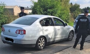 droga gminna, widoczna kolumna samochodów i radiowozy policji, policjanci kontrolują samochody i legitymują pseudokibiców.