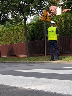 Policjant stoi przed znakiem przy przejściu dla pieszych.