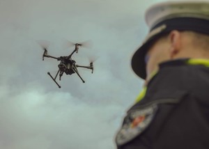 latający dron , w kadrze także sterujący nim policjant