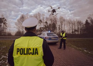 Dwóch umundurowanych policjantów, dron i radiowóz.